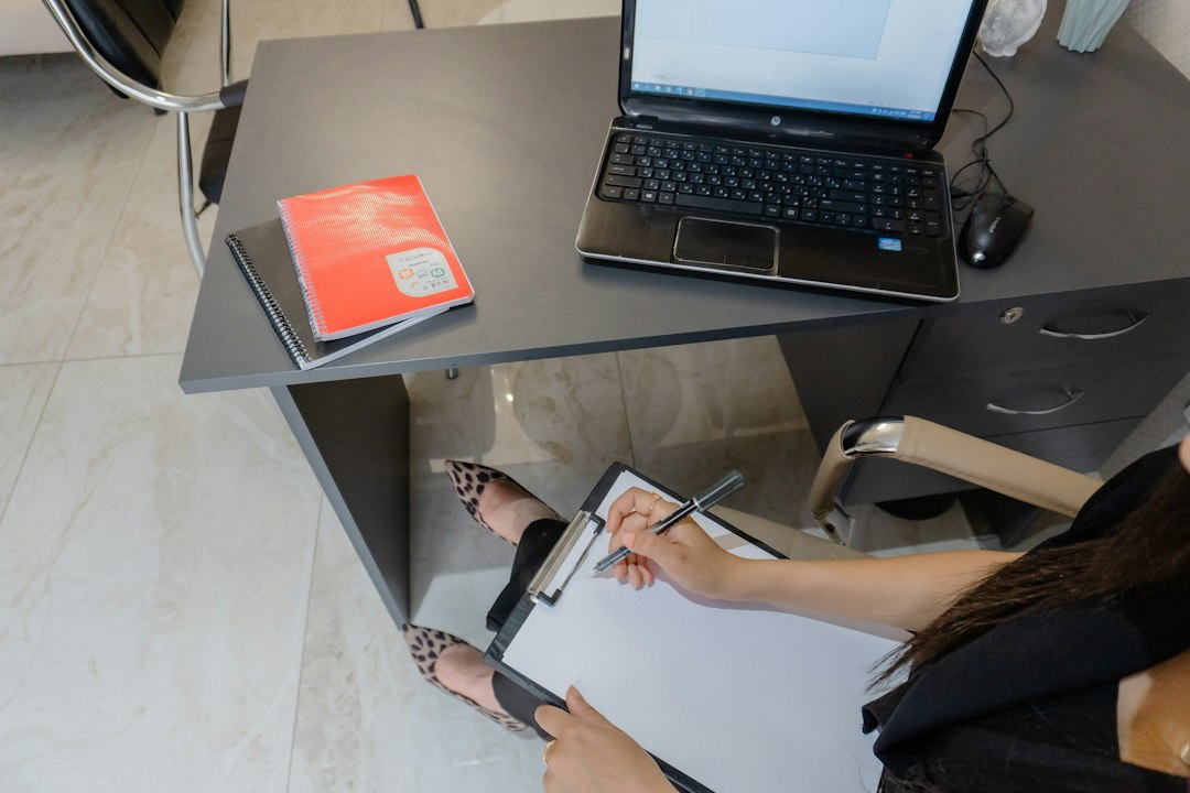 A person writing on a clipboard at a desk beside an open laptop — recording what to capture for each use case