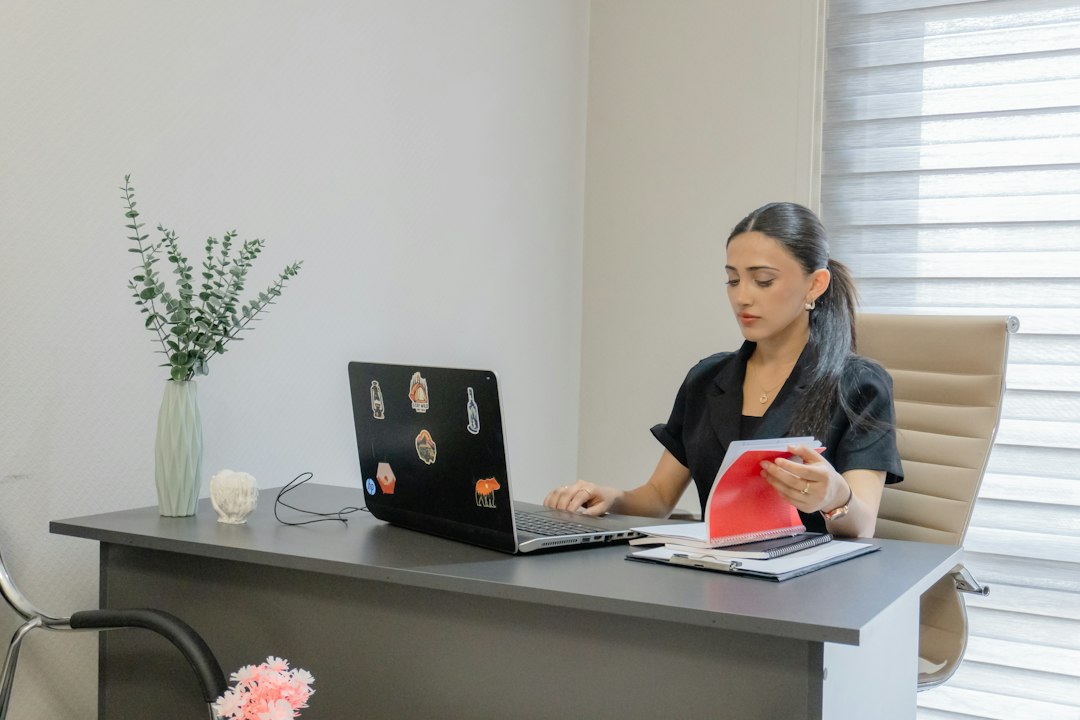 A professional reviewing a document at her desk with a laptop open in front of her