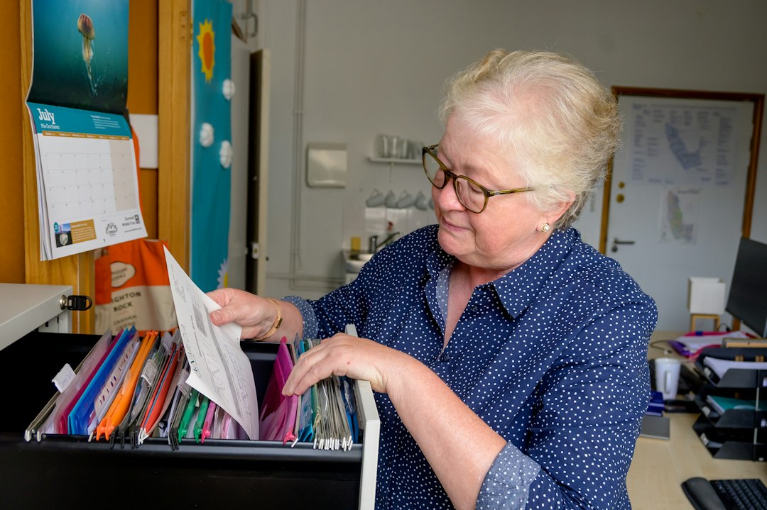 A coordinator sorts through folders in an open filing drawer, gathering evidence that lives across the department