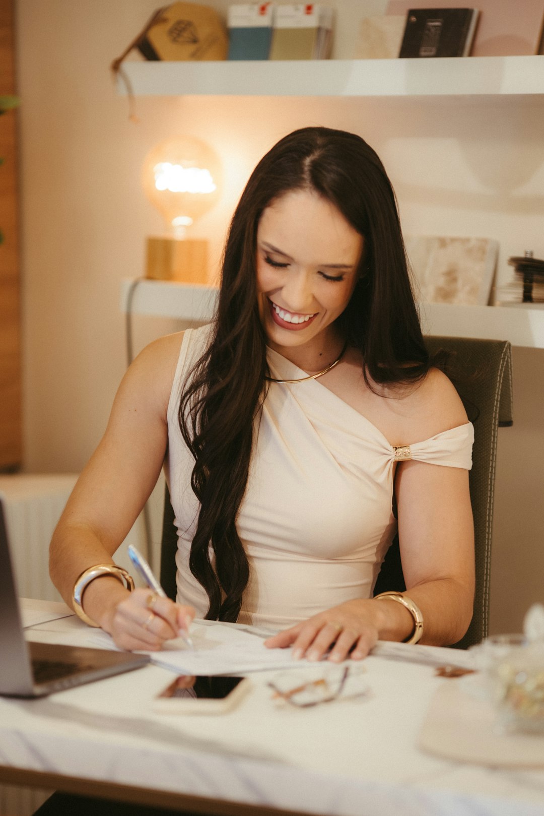 A student writing notes at a desk with a laptop